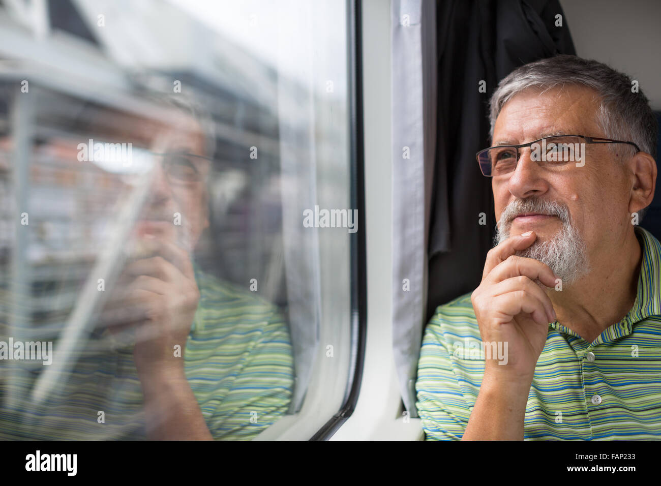 Senior man enjoying a train travel - leaving his car at home, he savours the time spent travelling, looks out of the window, has Stock Photo