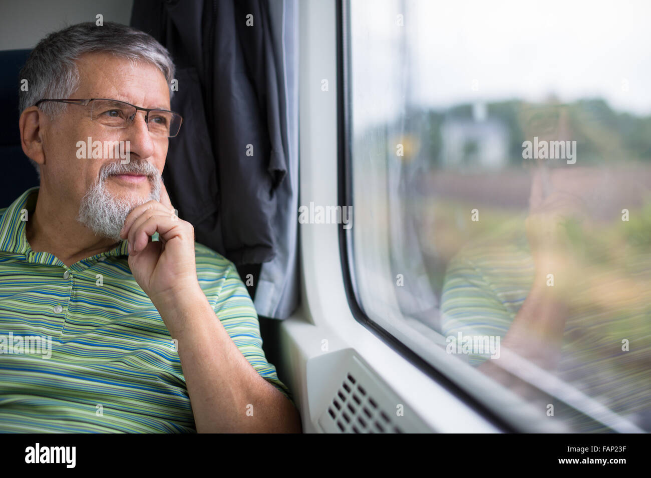 Senior man enjoying a train travel - leaving his car at home, he savours the time spent travelling, looks out of the window Stock Photo