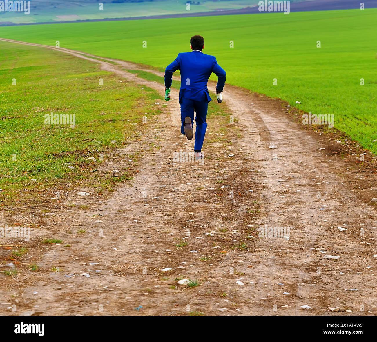groom in blue suit running away with beer bottles on a field path Stock