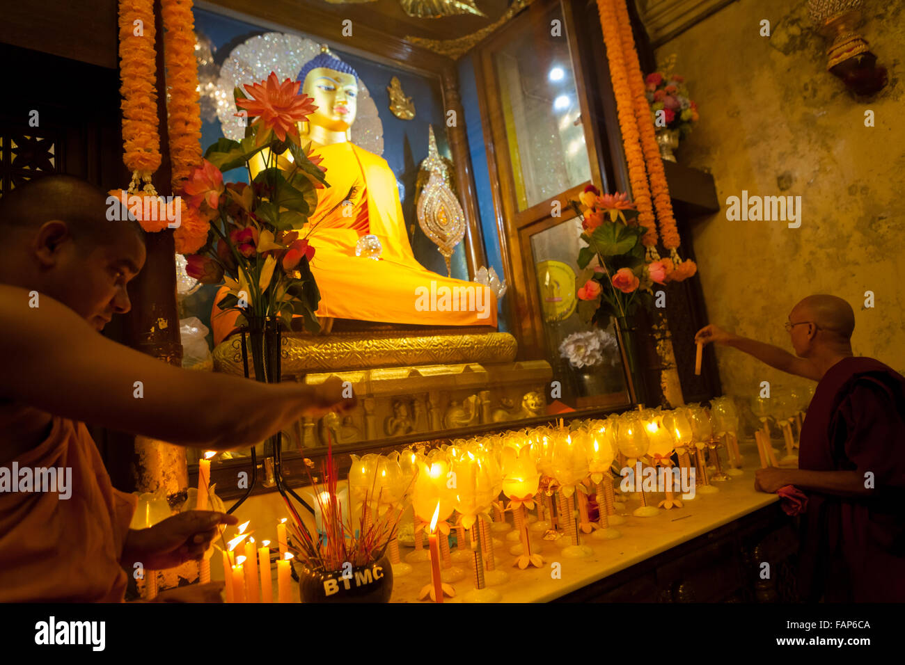 Monks offering praying candles in front of golden Buddha statue inside