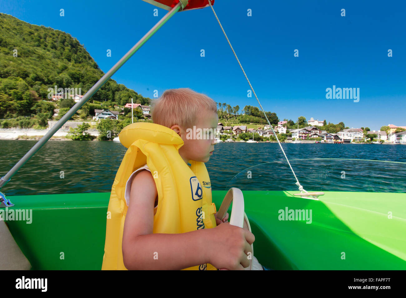 Little boy drives water boat on alpine lake. Stock Photo