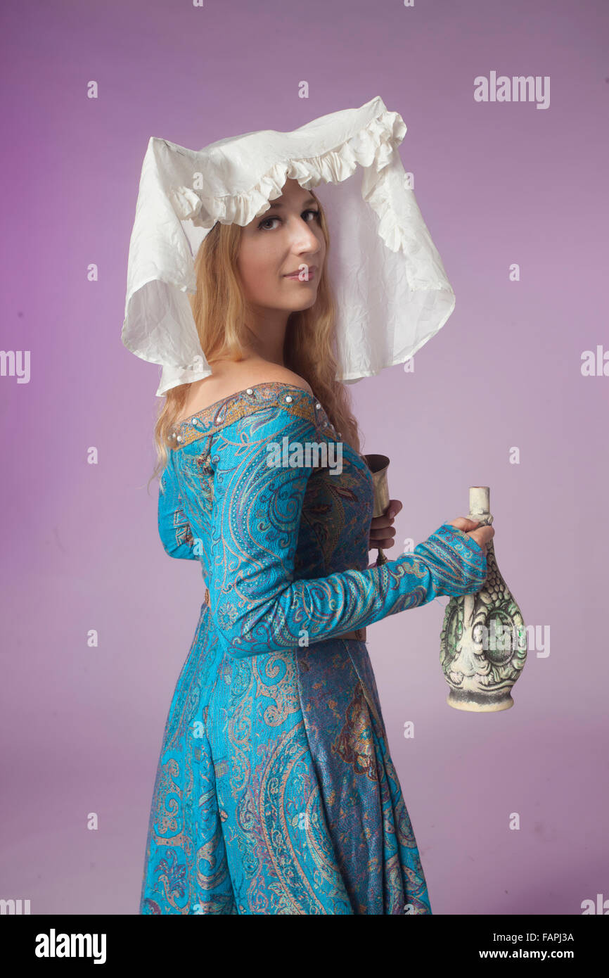 Studio shot of beautiful girl dressed as a medieval noblewoman half-turned holding a jar (on purple background) Stock Photo