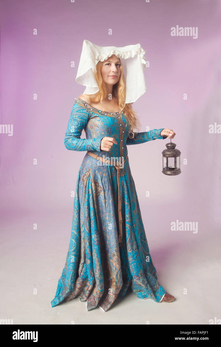 Studio shot of beautiful girl dressed as a medieval noble lady holding a retro style lamp on purple background Stock Photo