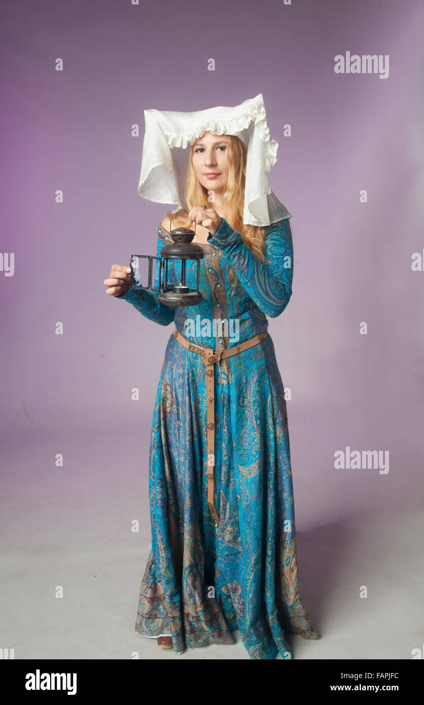 Studio shot of beautiful girl dressed as a medieval lady holding a retro style lamp on purple background Stock Photo