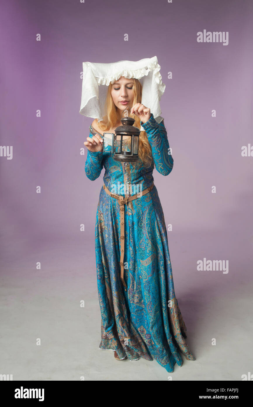 Studio shot of beautiful girl dressed as a medieval lady outing a retro style lamp on purple background Stock Photo