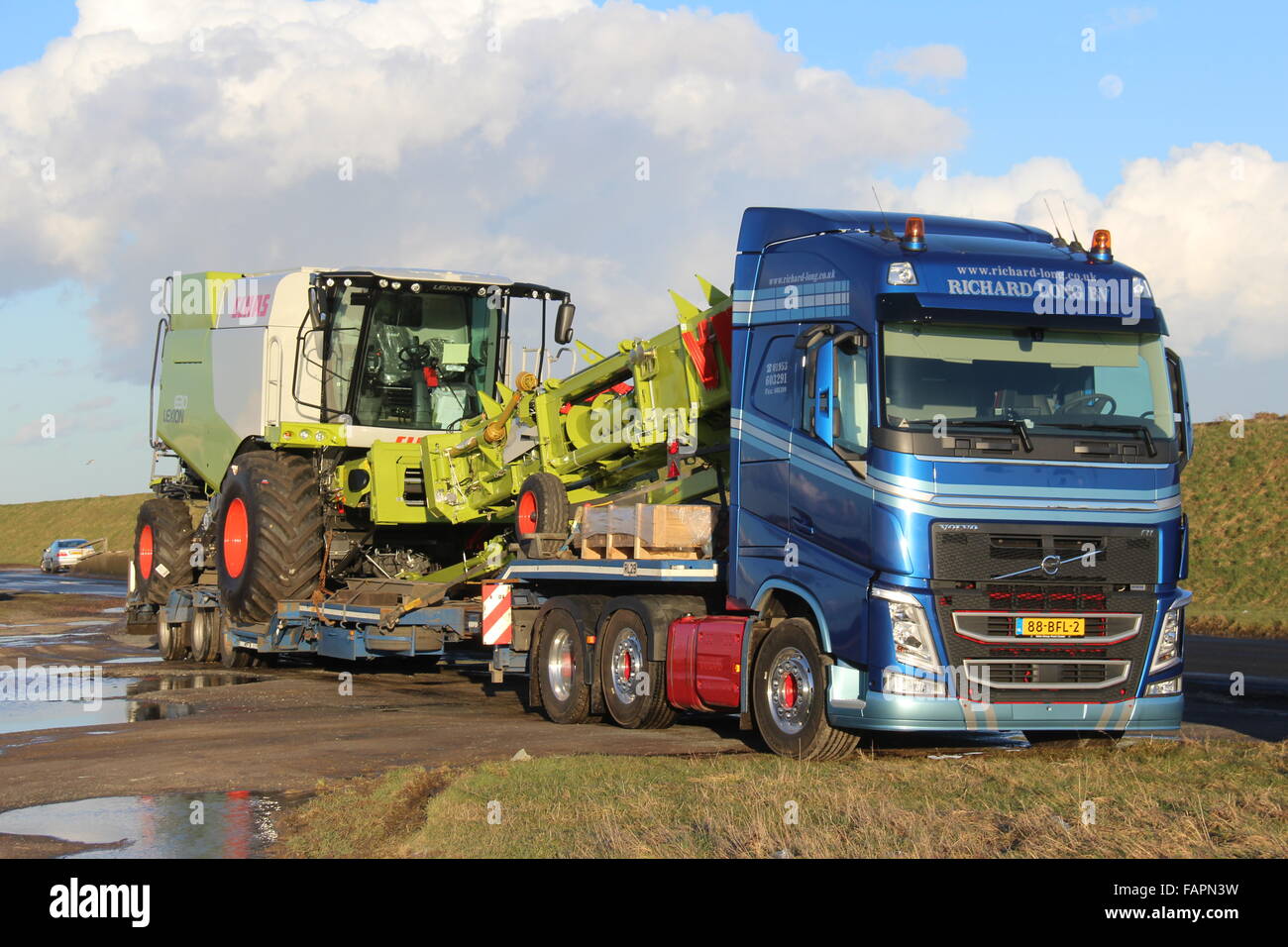A BLUE VOLVO TRUCK FROM THE NETHERLANDS DELIVERING A BRAND NEW GREEN COMBINE HARVESTER TO A UK FARM Stock Photo