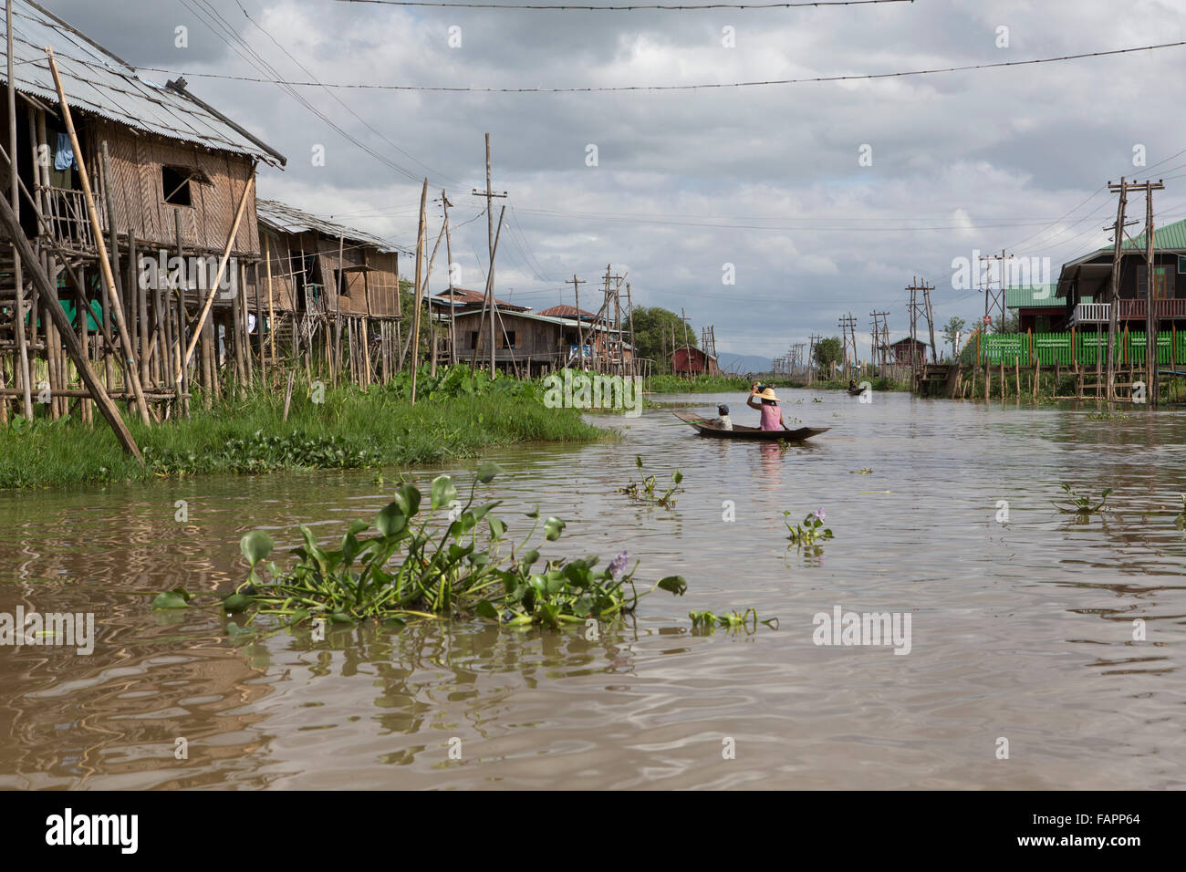 A woman rows between stilted houses at Nyaungshwe on Inle Lake in Myanmar (Burma). The water level rises and falls markedly duri Stock Photo
