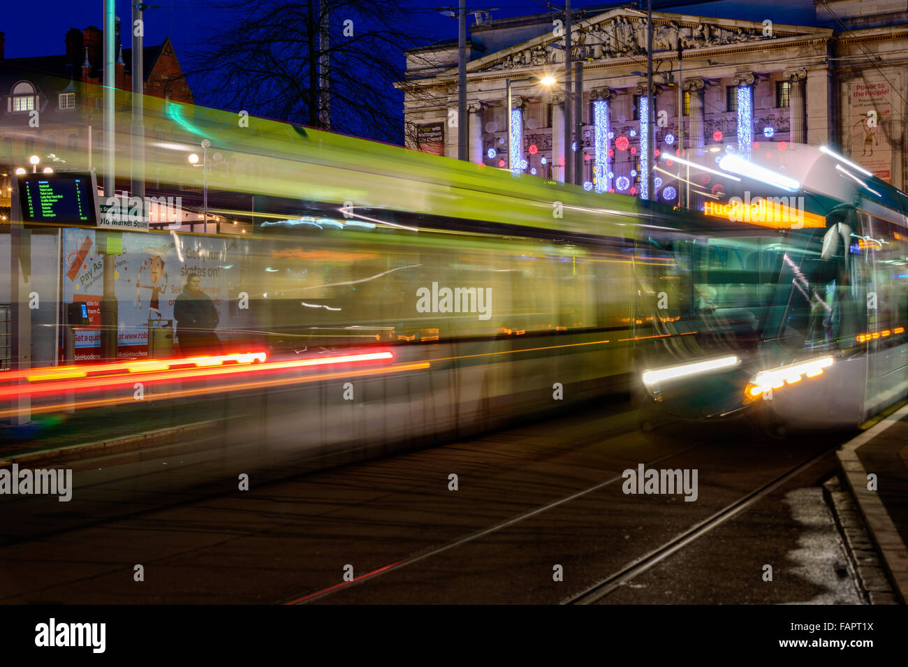 Two Nottingham trams, blurred in motion, pass each other in the market square at Christmas In Nottingham. Stock Photo