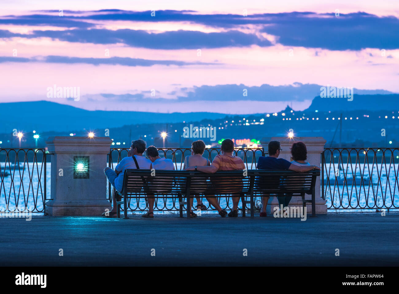 Syracuse Sicily bay, on a summer evening a group of tourists watch the remains of a colourful sunset over the harbour in Syracuse, Sicily. Stock Photo