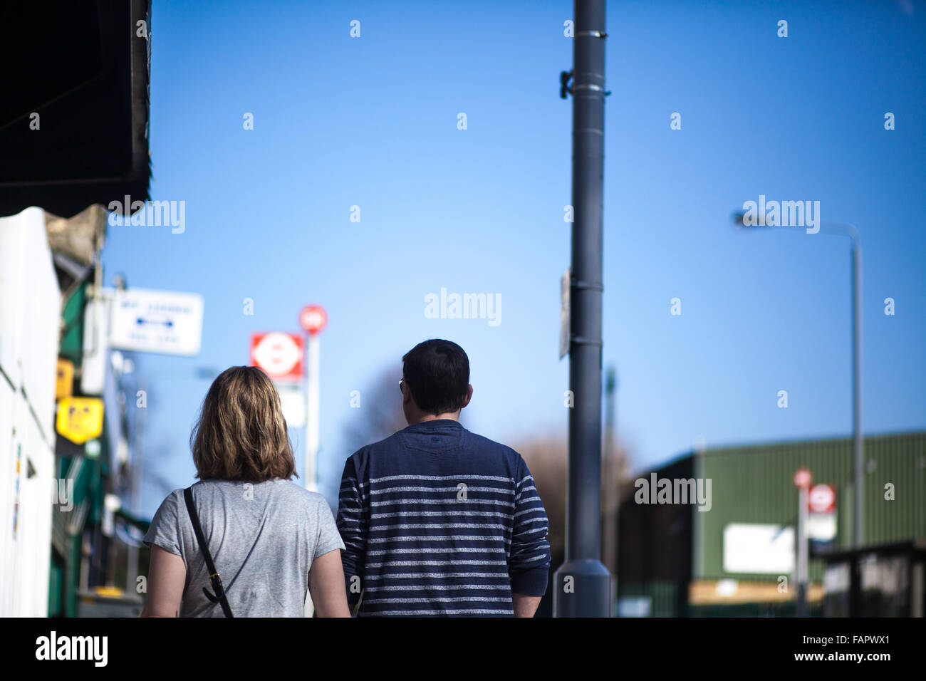 Man and woman walking down street with bus stops and blue sky in distance. Stock Photo