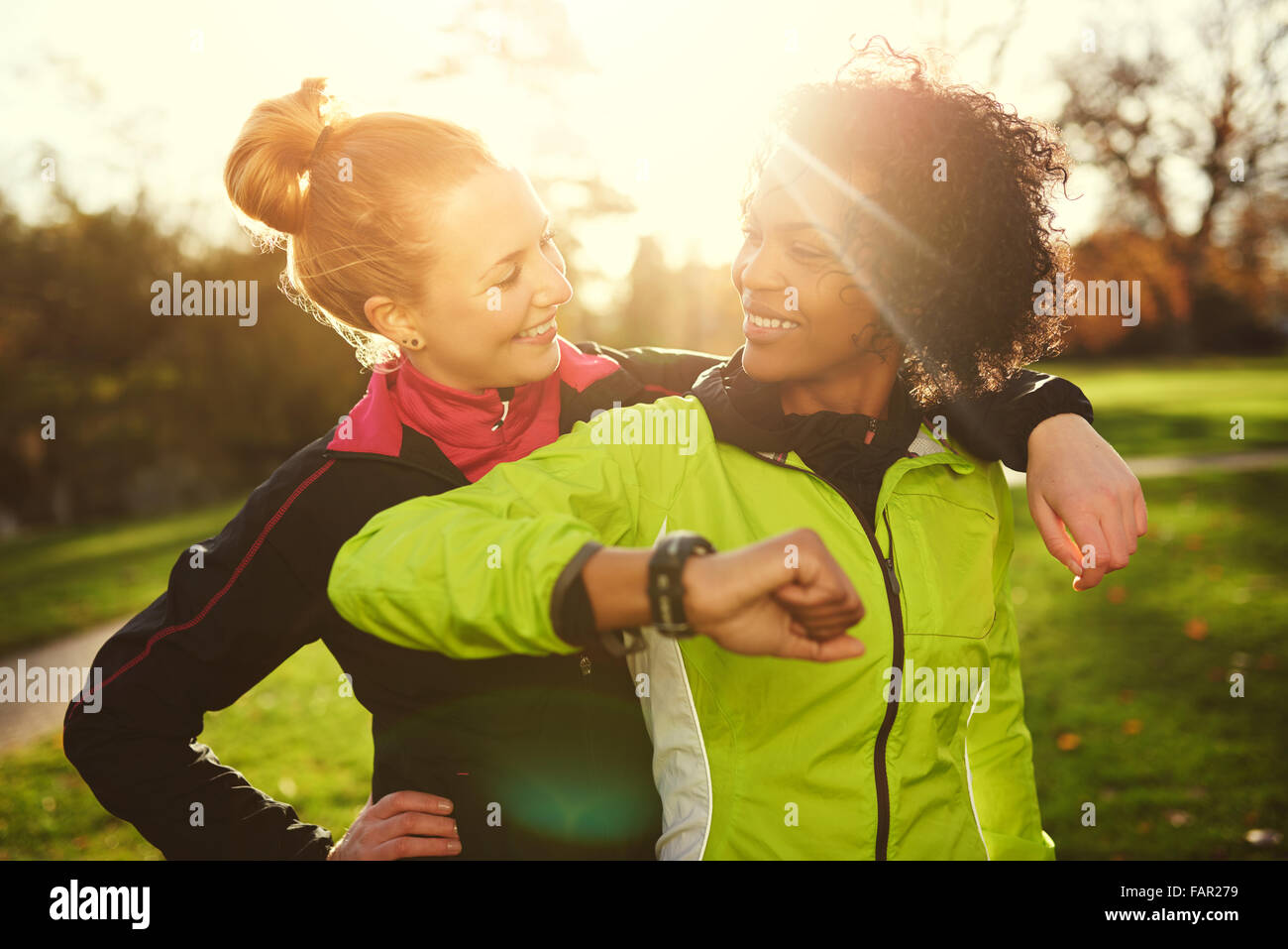 Two girlfriends in sportswear looking at each other while hugging in sunny park after workout Stock Photo
