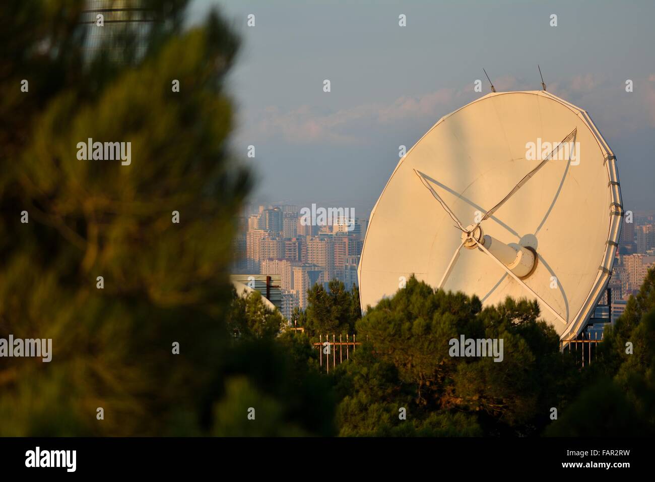 Large white satellite dish behind trees with a view of Baku, capital of Azerbaijan, in the background Stock Photo