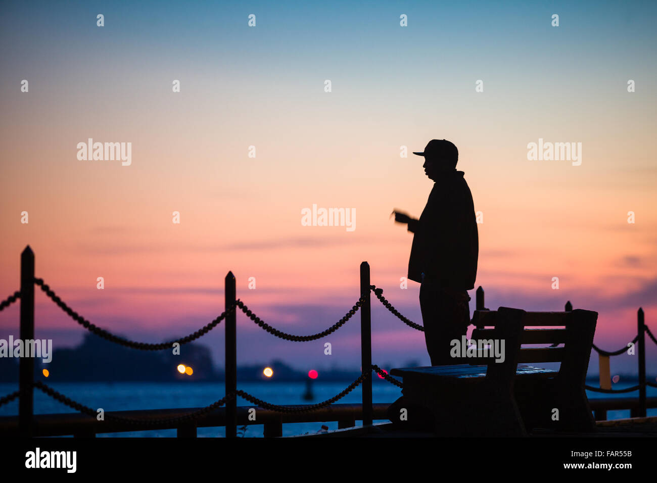 One man standing silhouetted against the sunset along the waterfront. Stock Photo