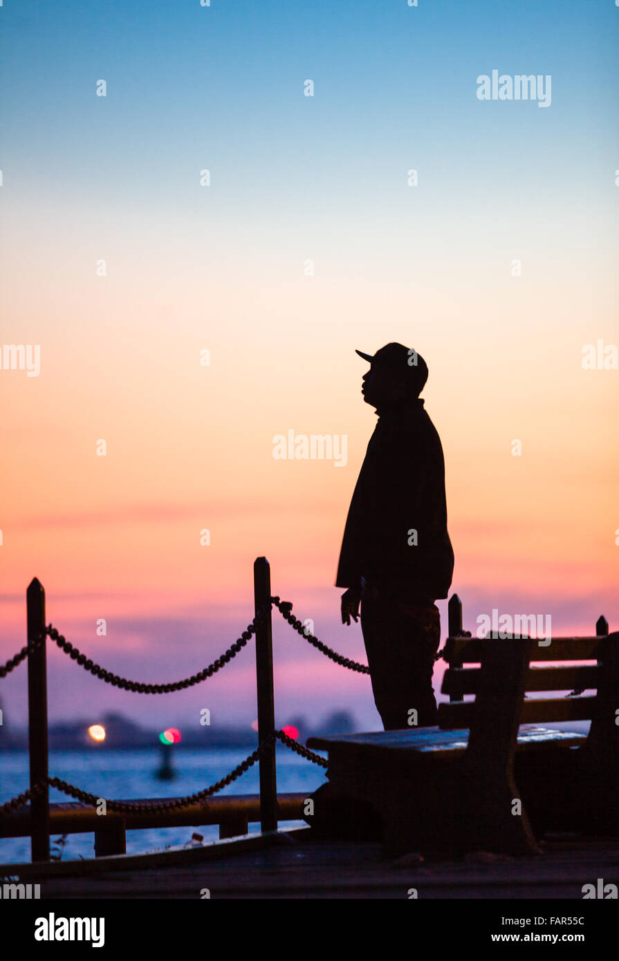 One man standing silhouetted against the sunset along the waterfront. Stock Photo