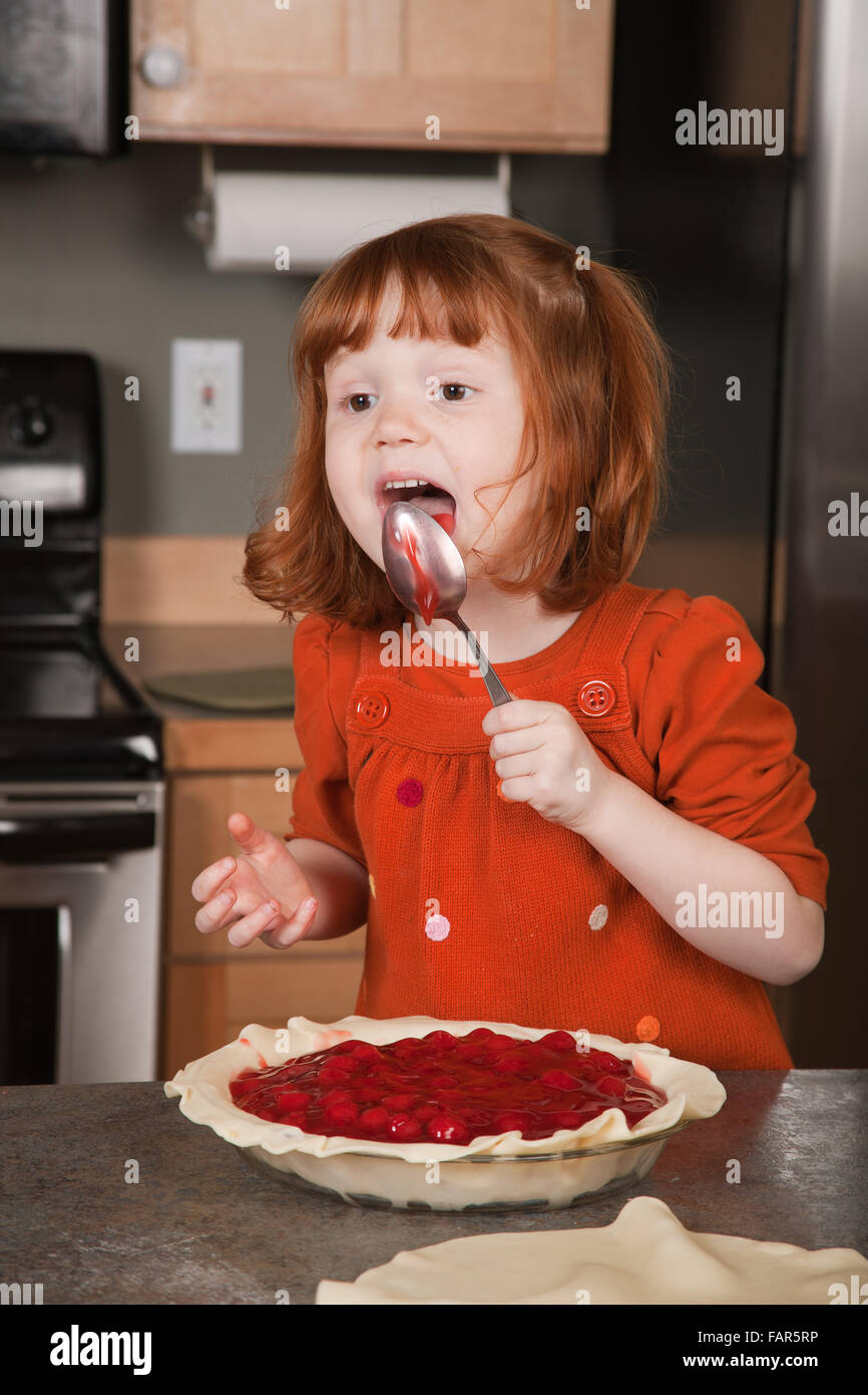 Four year old girl licking spoon from filling a cherry pie Stock Photo