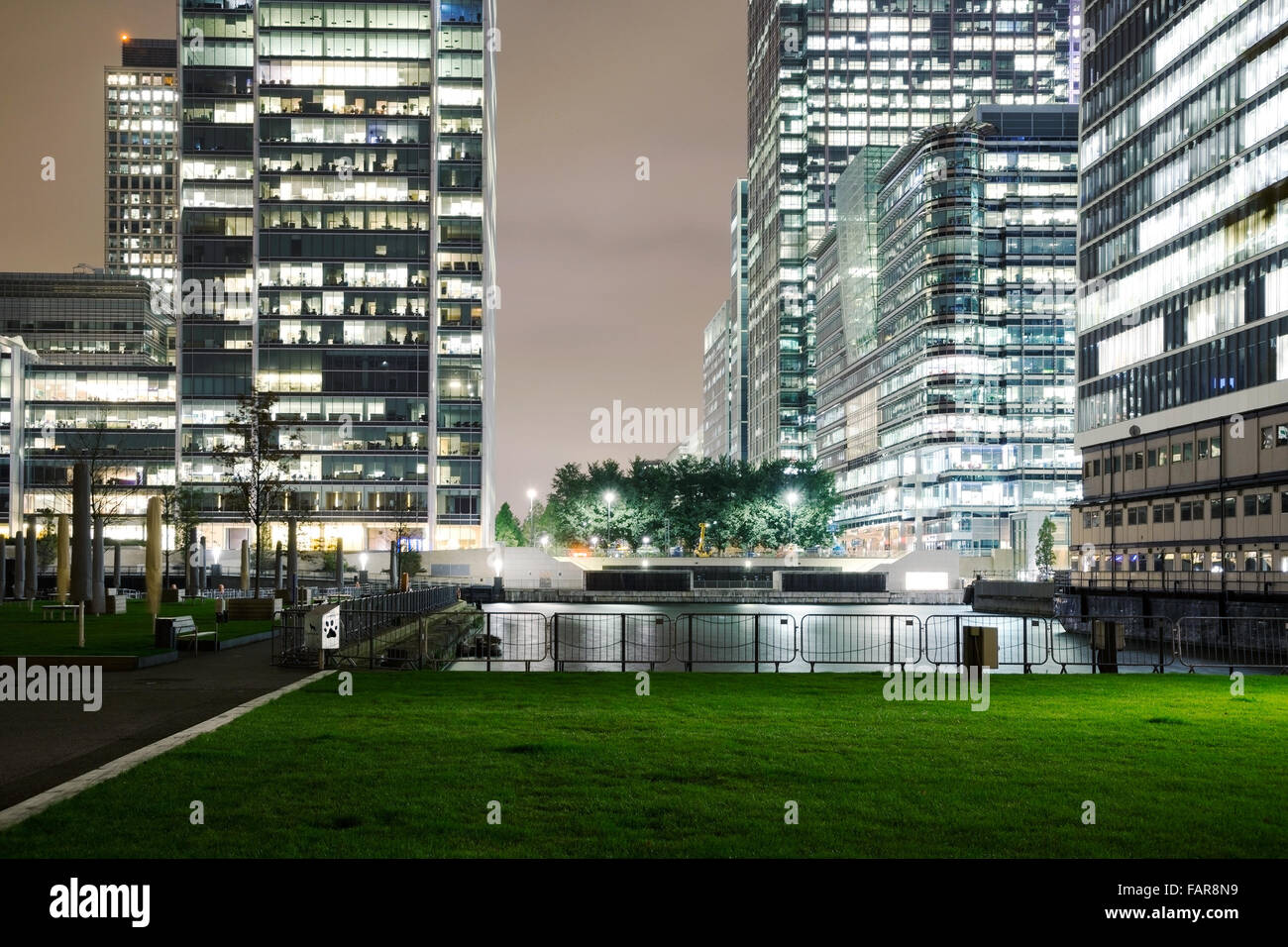 Canary Wharf offices with lights on at night time with a public park area in the foreground Stock Photo