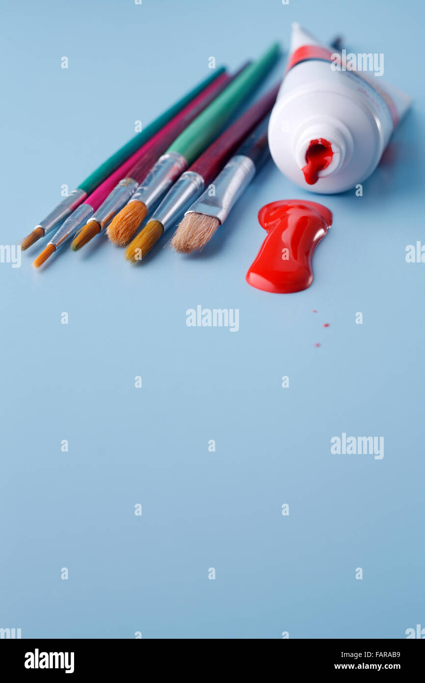 Multiple paintbrushes with a tube of paint isolated on blue background ...