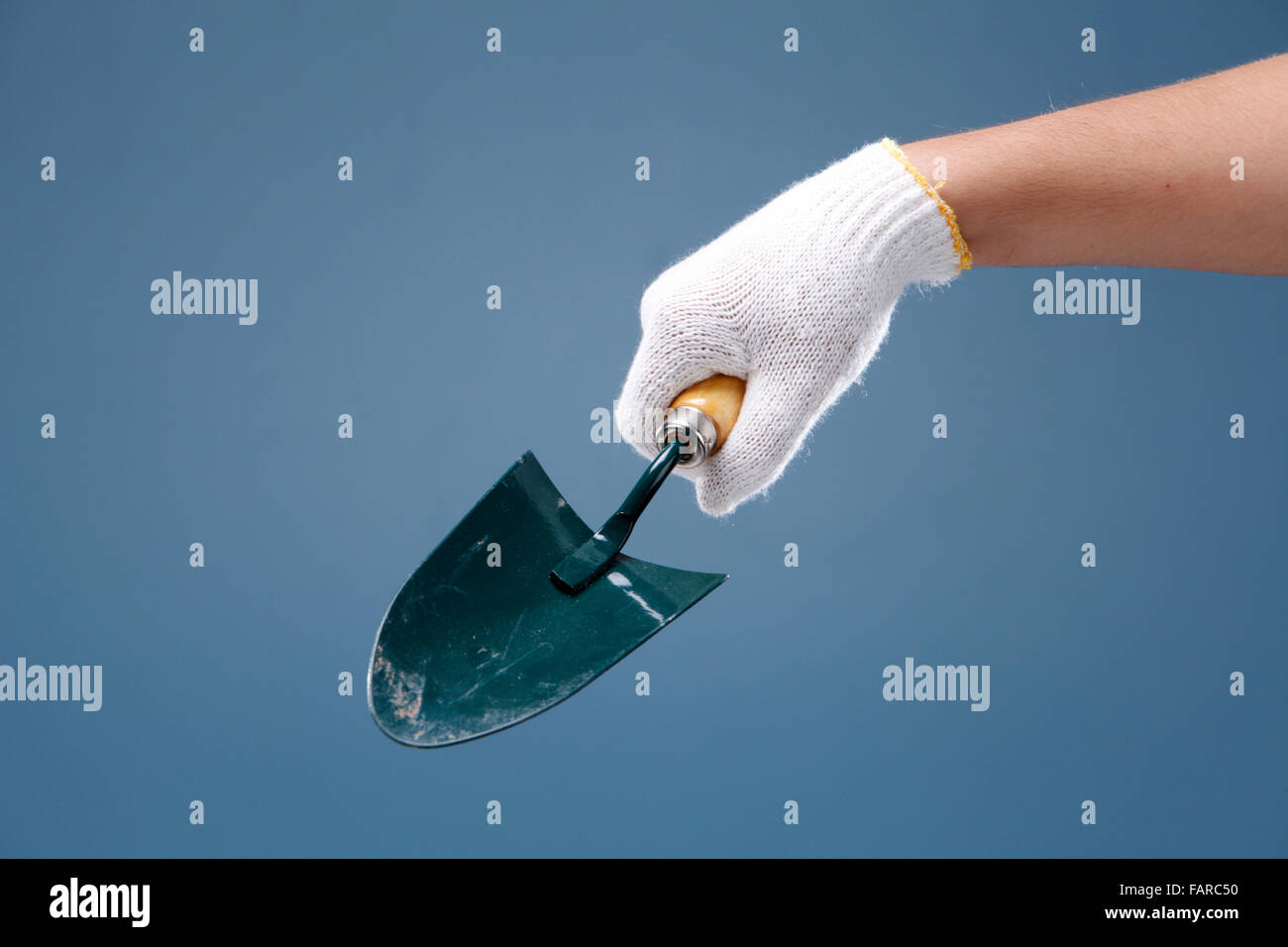 Hand holding garden trowel on coloured background. Stock Photo