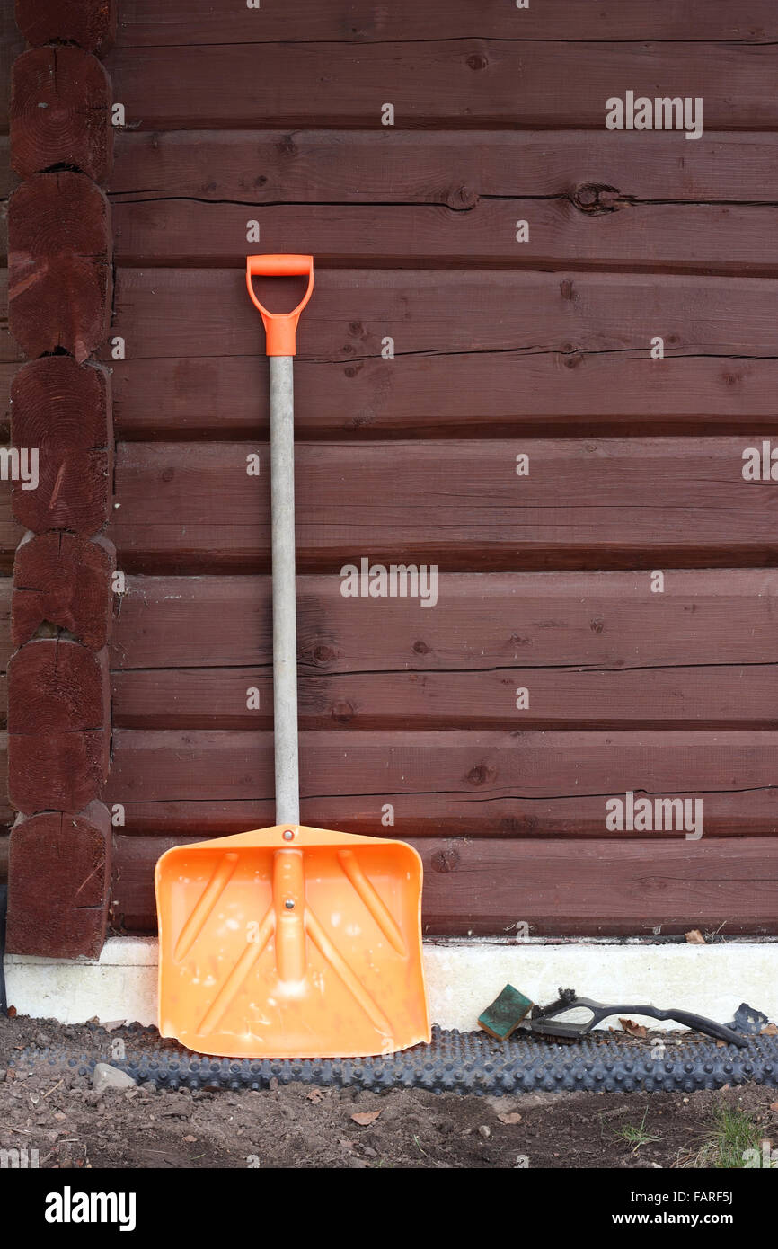 The big shovel for cleaning of snow is leaned against a wall of a wooden rural shed Stock Photo