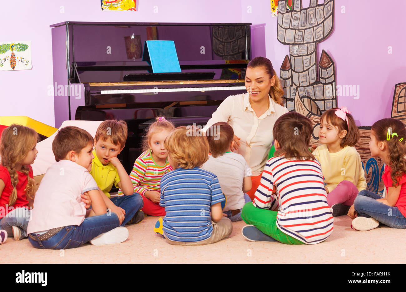 Group of kids sit and listen to teacher tell story Stock Photo