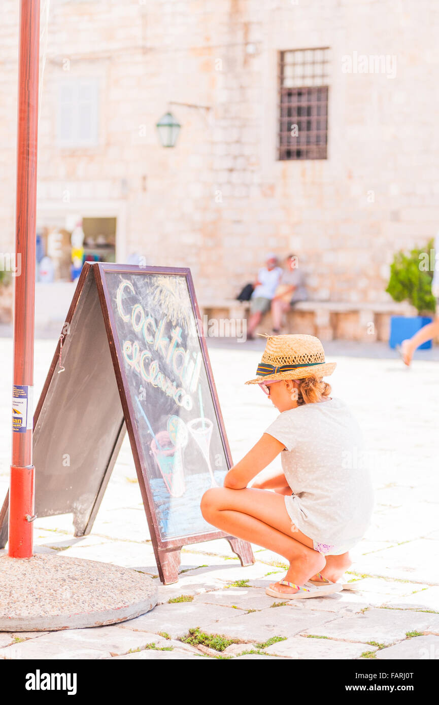 Little girl on holiday reads the chalk board outside a restaurant bar in Hvar Island, Croatia, Europe. Stock Photo