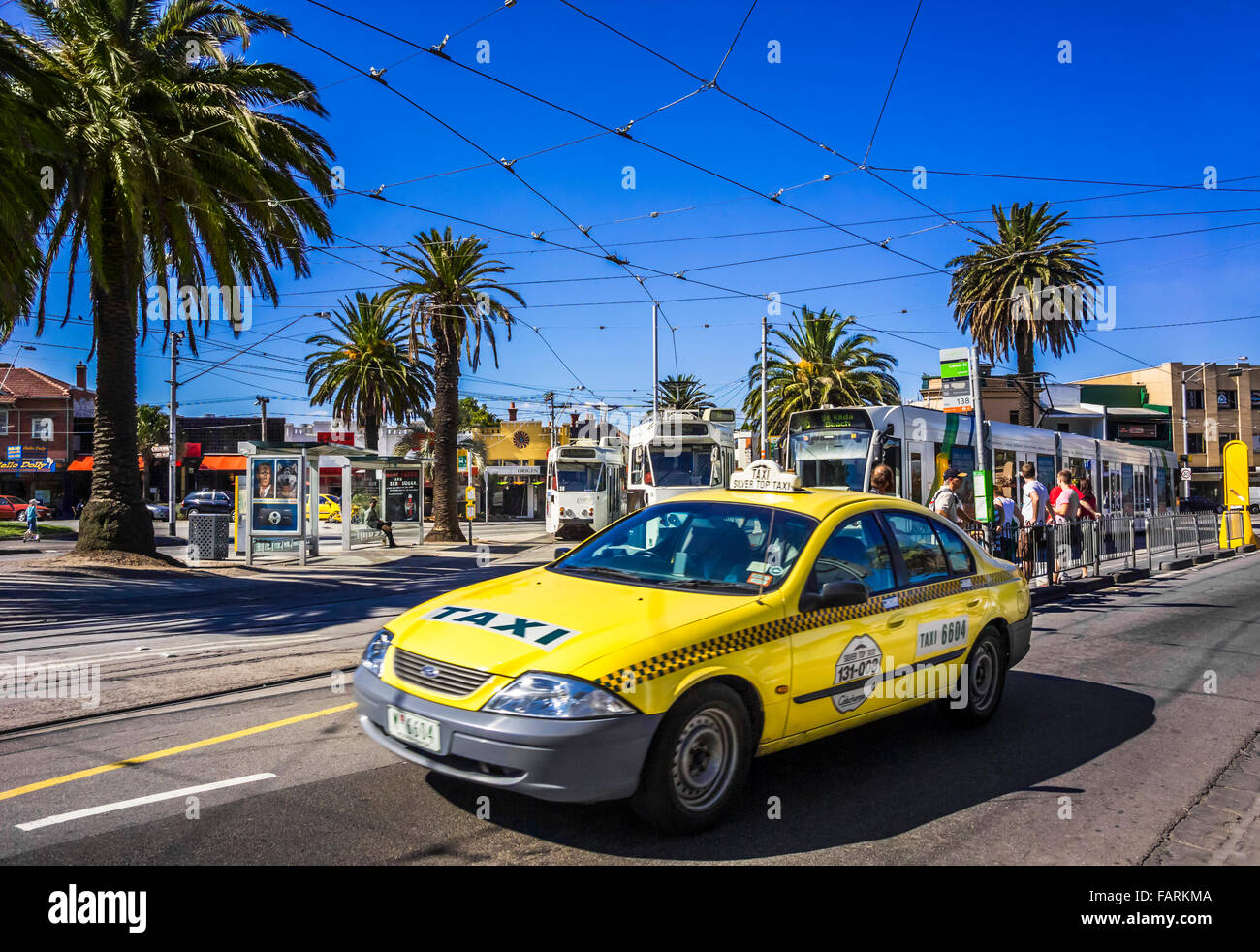 Yellow taxi cab on St Kilda street with palm trees and trams in background, Melbourne Australia