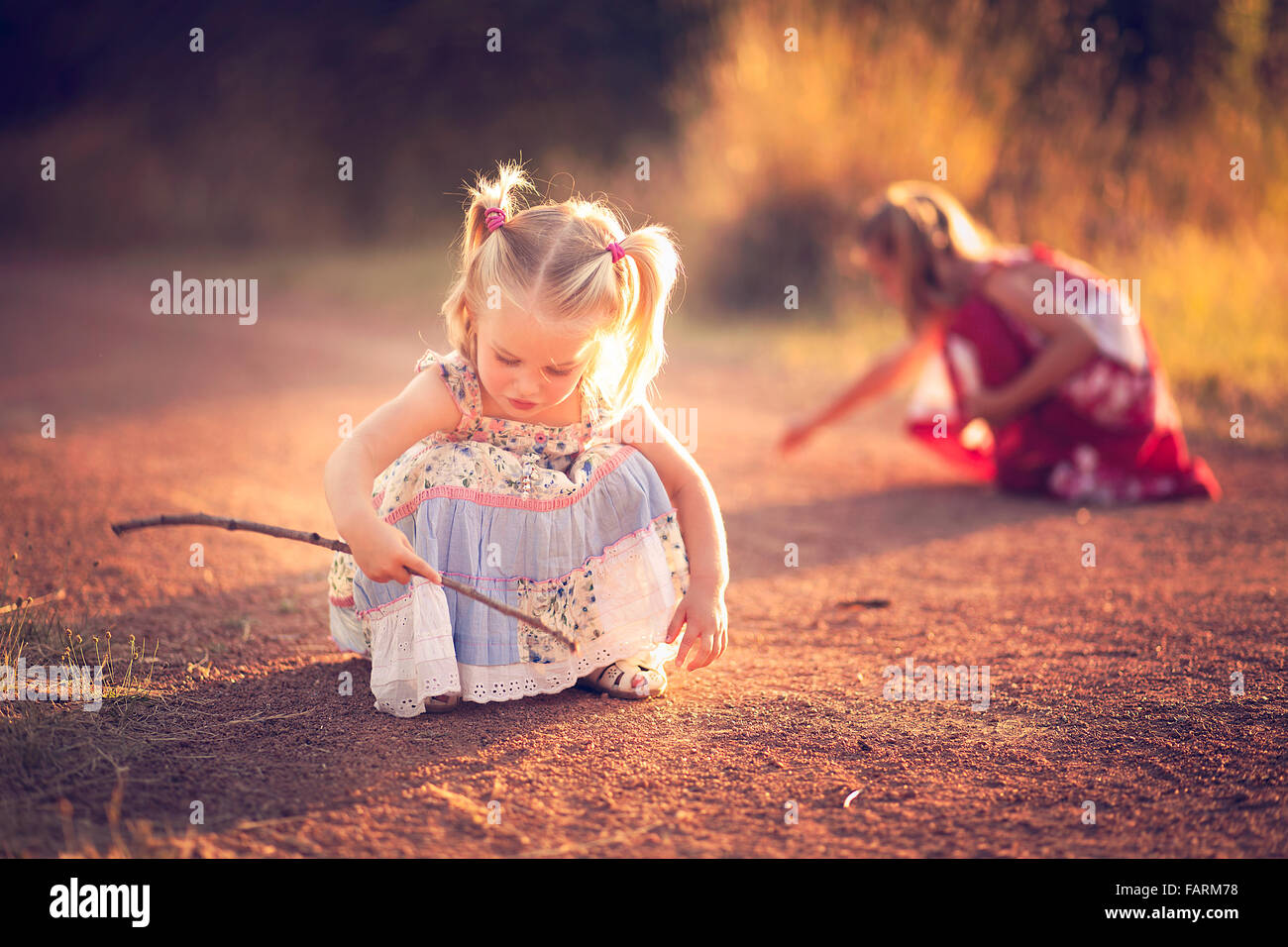 Little girl playing in the dirt with a stick Stock Photo