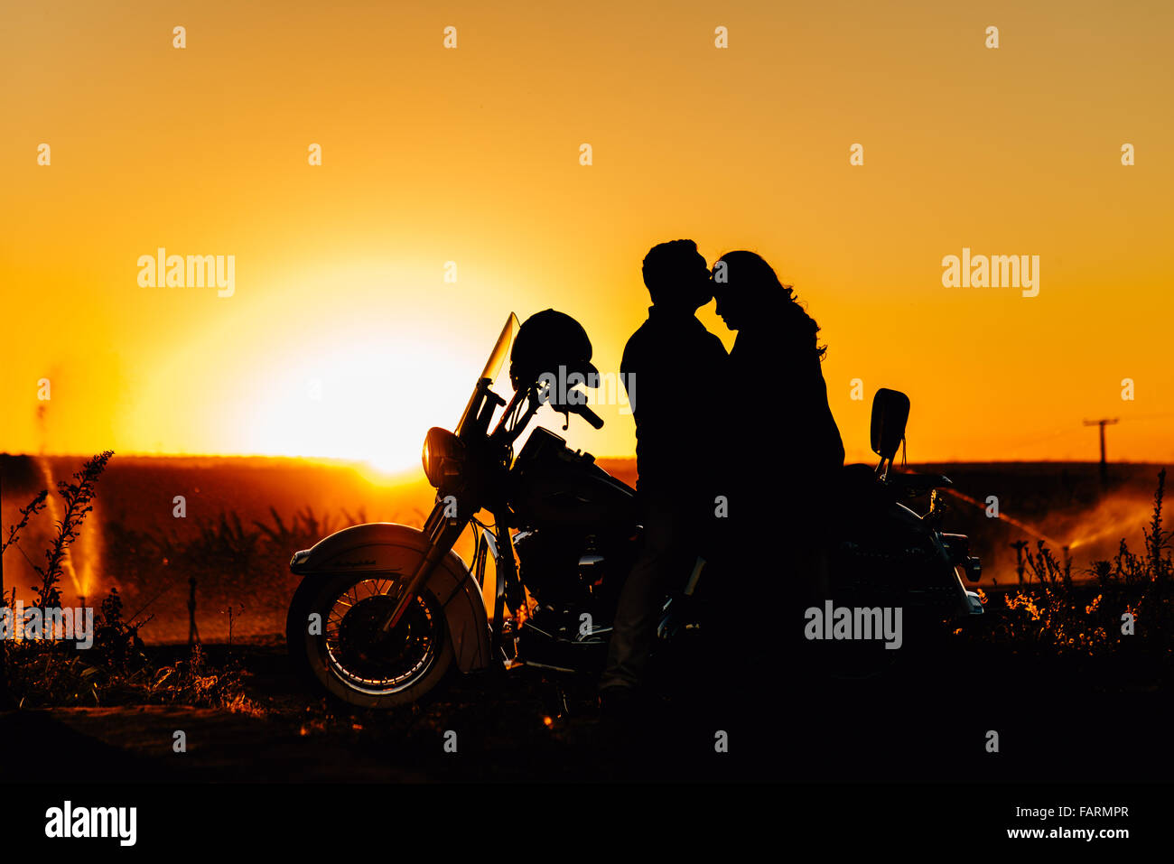 couple kissing on a motorcycle harley davidson with sunset in the background Stock Photo