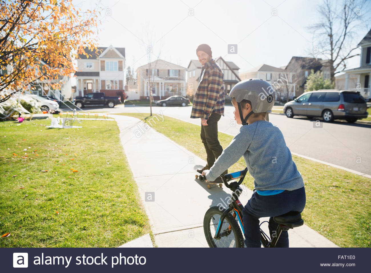 Father skateboarding and son riding bike neighborhood sidewalk Stock Photo
