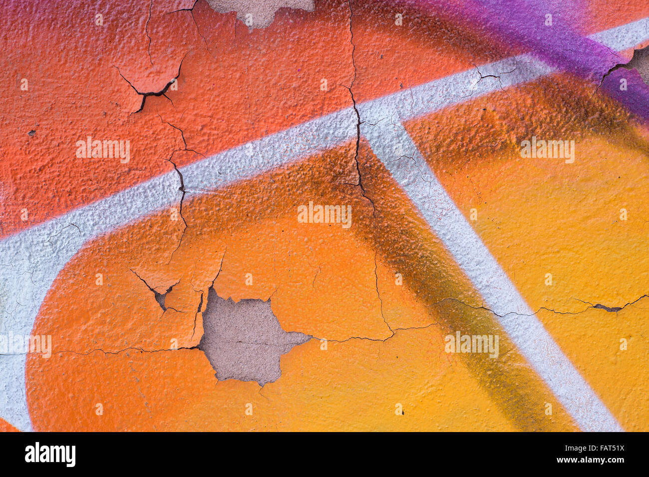 Closeup of a peeling and cracked wall with orange violet, and white spray drawings Stock Photo
