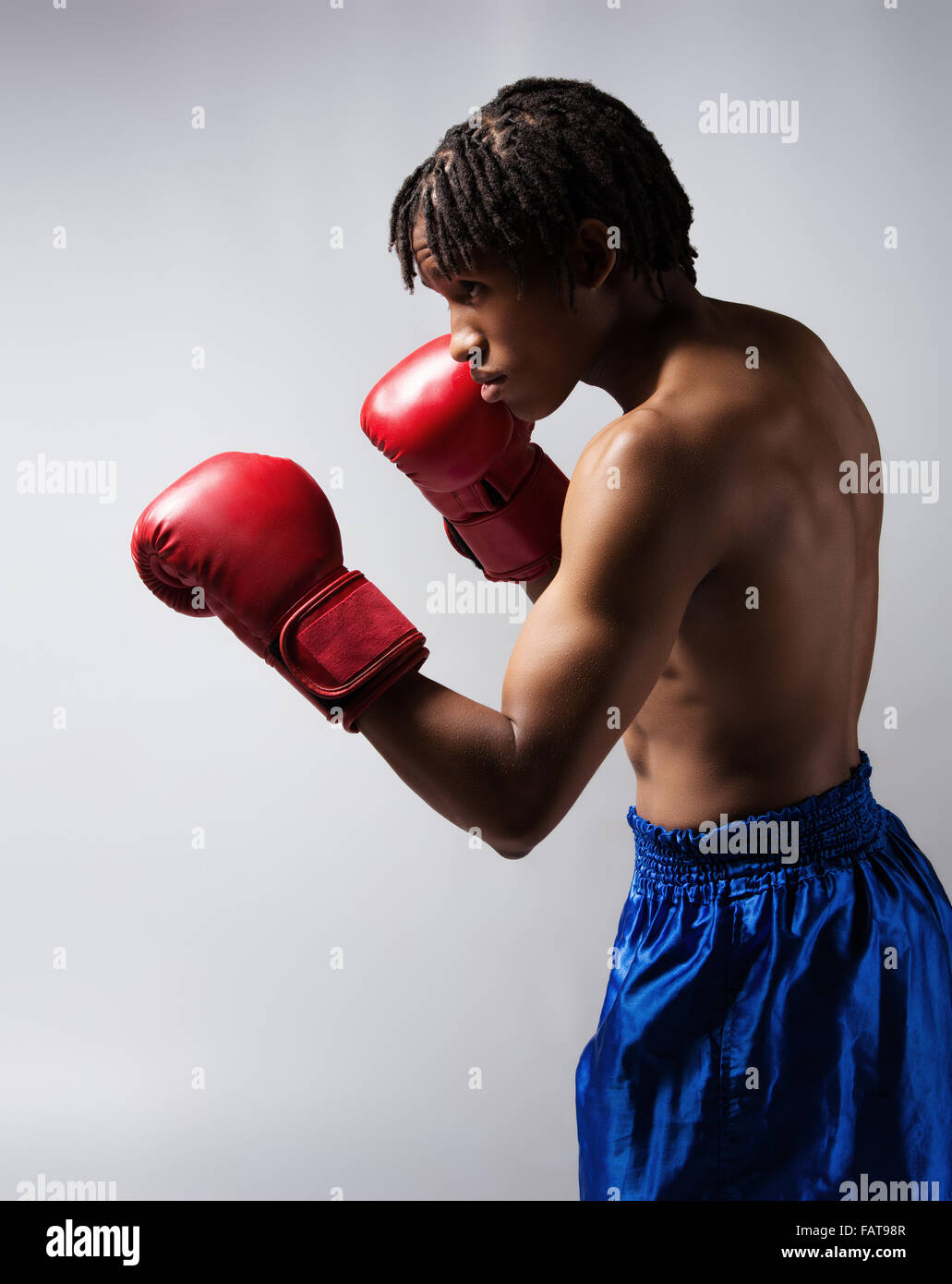 Young muscular athletic male boxer wearing blue boxing shorts and red boxing gloves. Stock Photo