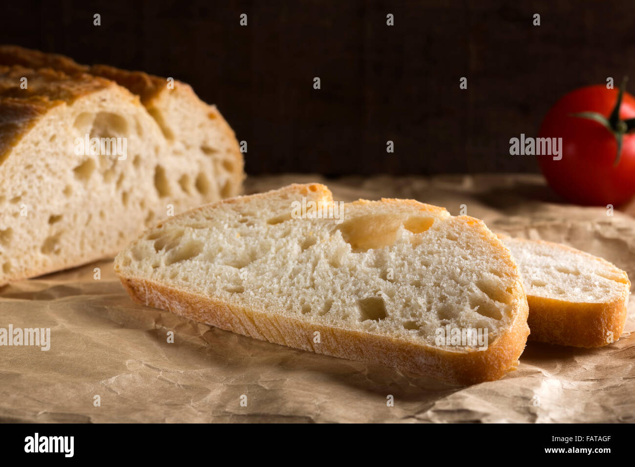 Sliced fresh white bread with browned crust and tomato over paper Stock Photo