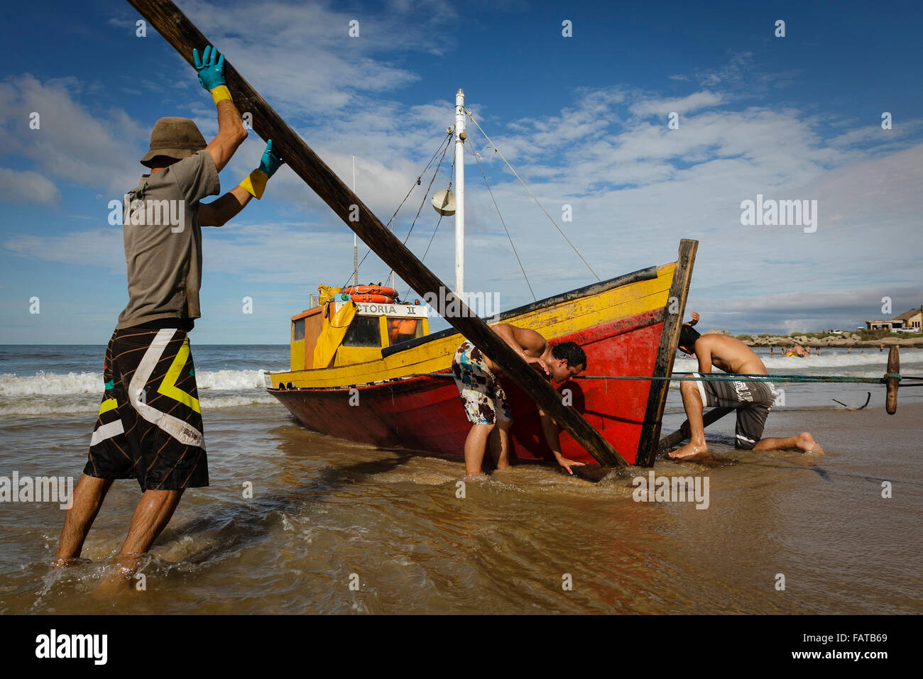 fisherman pushing the boat by hands among waves, using wooden  in Punta del Diablo. Uruguay Stock Photo