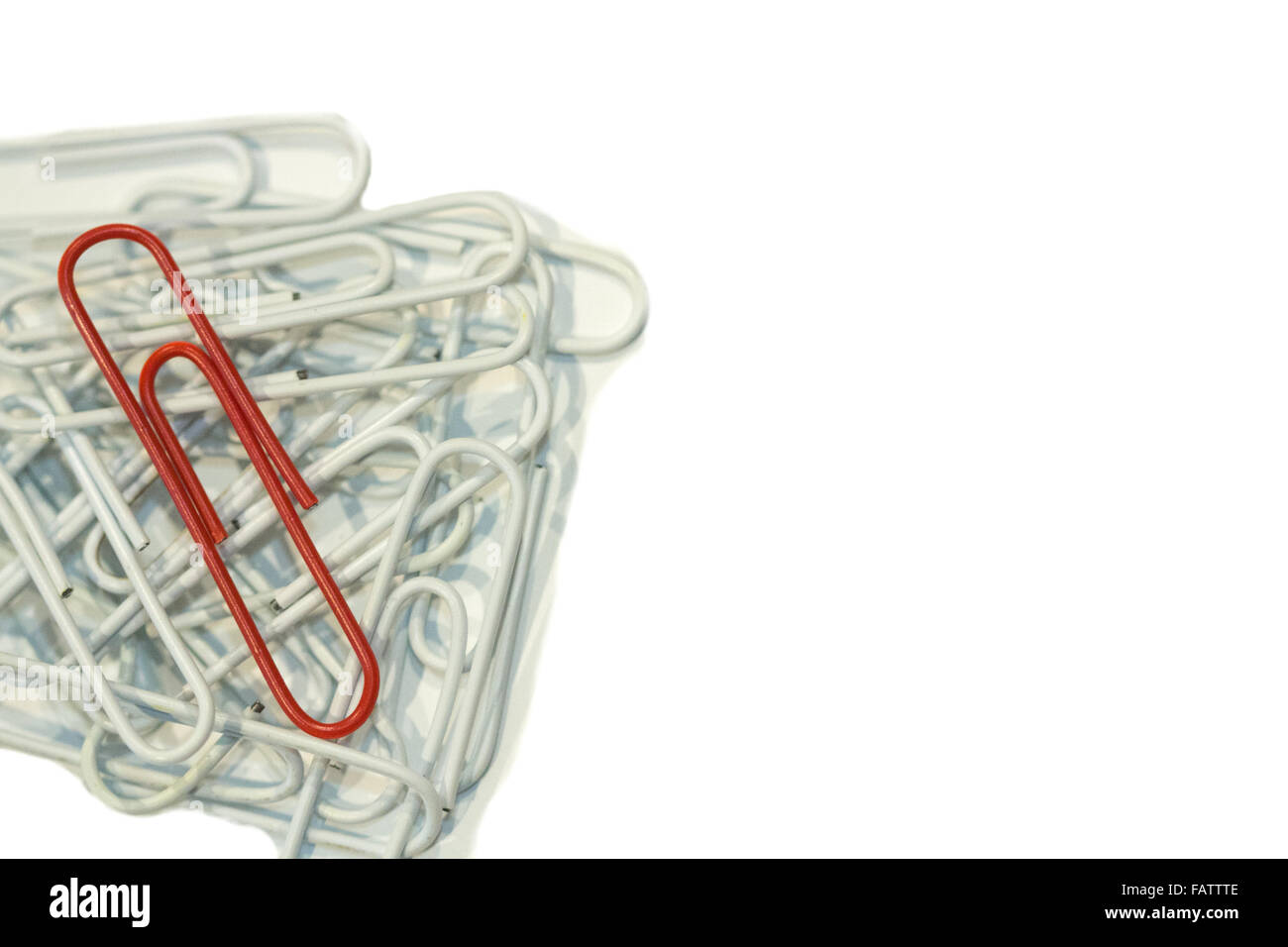 A red paper clip laying on top of a pile of white paper clips Stock Photo