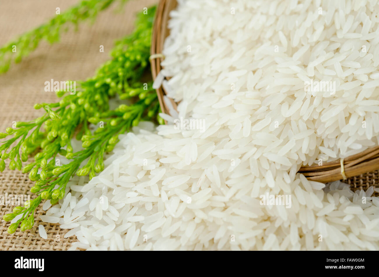 Jasmine rice in weave wooden basket with flower on sack background. Stock Photo