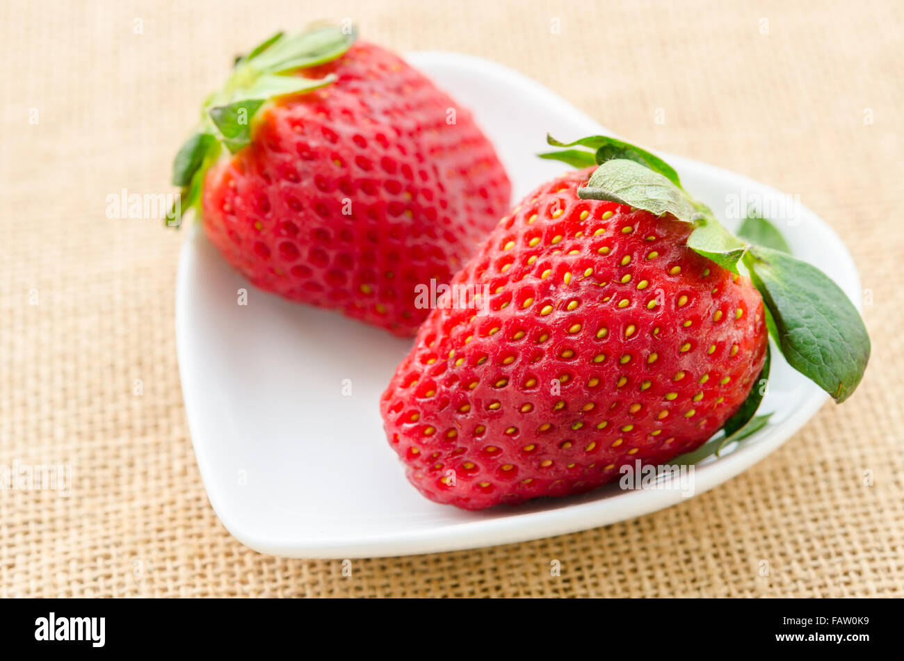 Ripe red strawberries in white cup heart shape on sack background. Stock Photo