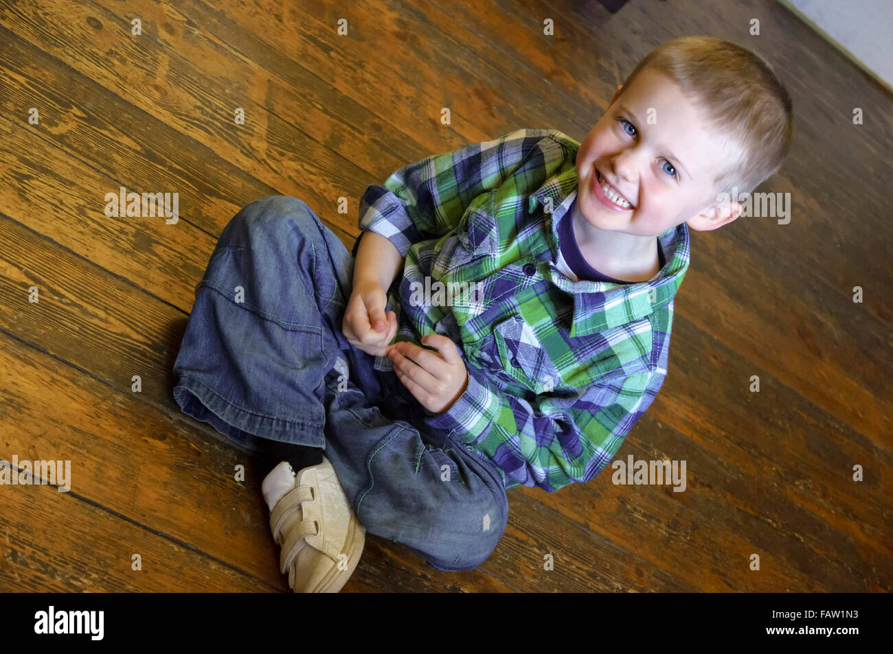 Smiling handsome young boy sitting on a wooden floor  Model Release: Yes.  Property Release: No. Stock Photo