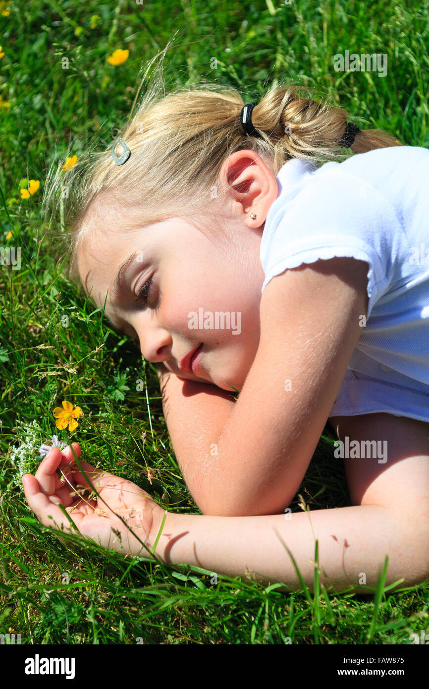 Young girl laying in grass thinking or daydreaming and looking at Buttercup flower  Model Release: Yes.  Property Release: No. Stock Photo