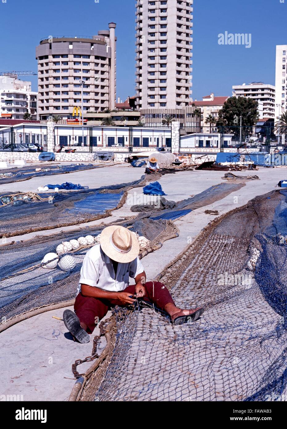Spanish fishermen sitting on floor mending their fishing nets in the harbour area, Fuengirola