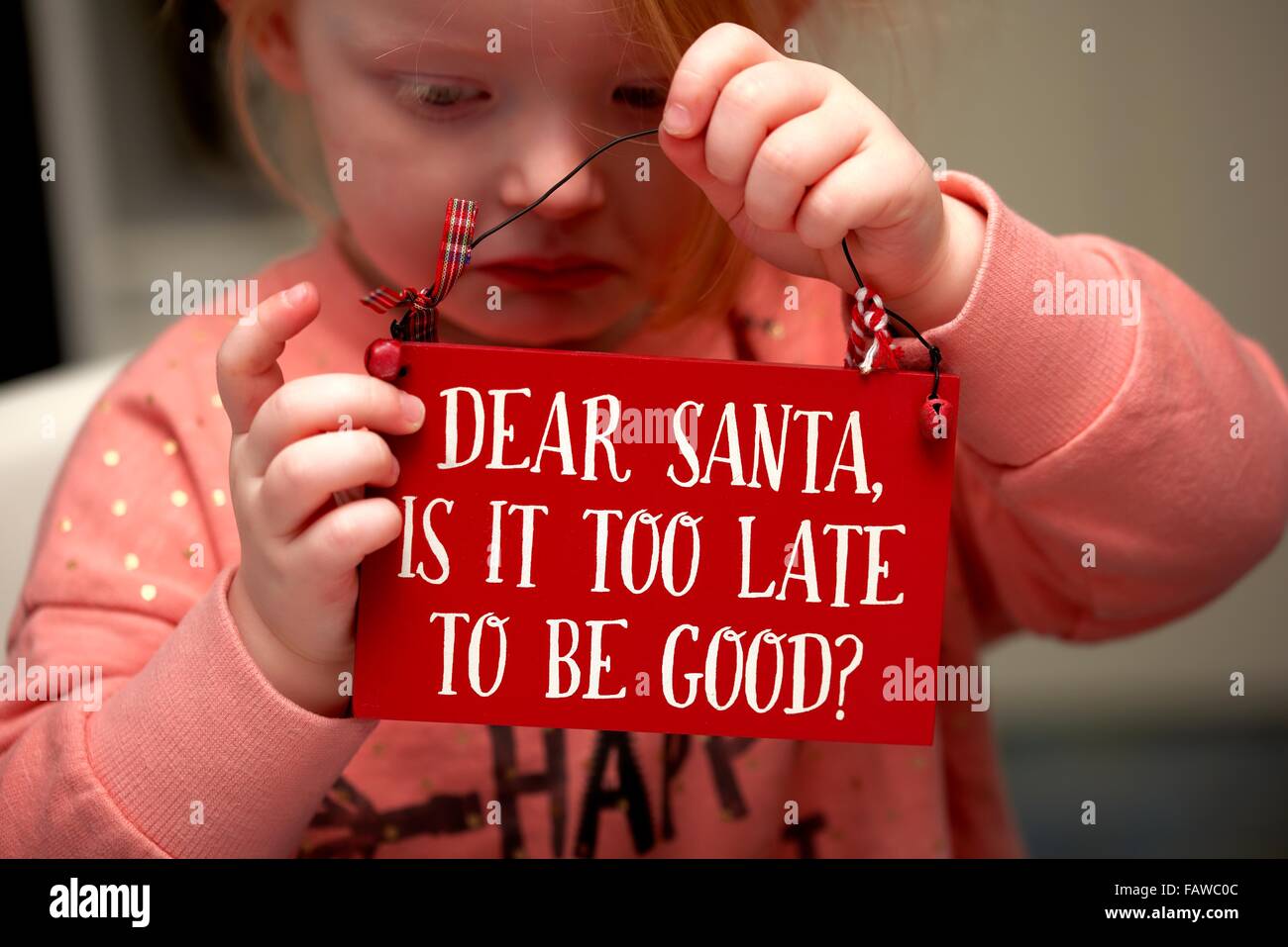 A 3 year old girl with a sad face holding a plaque with the message