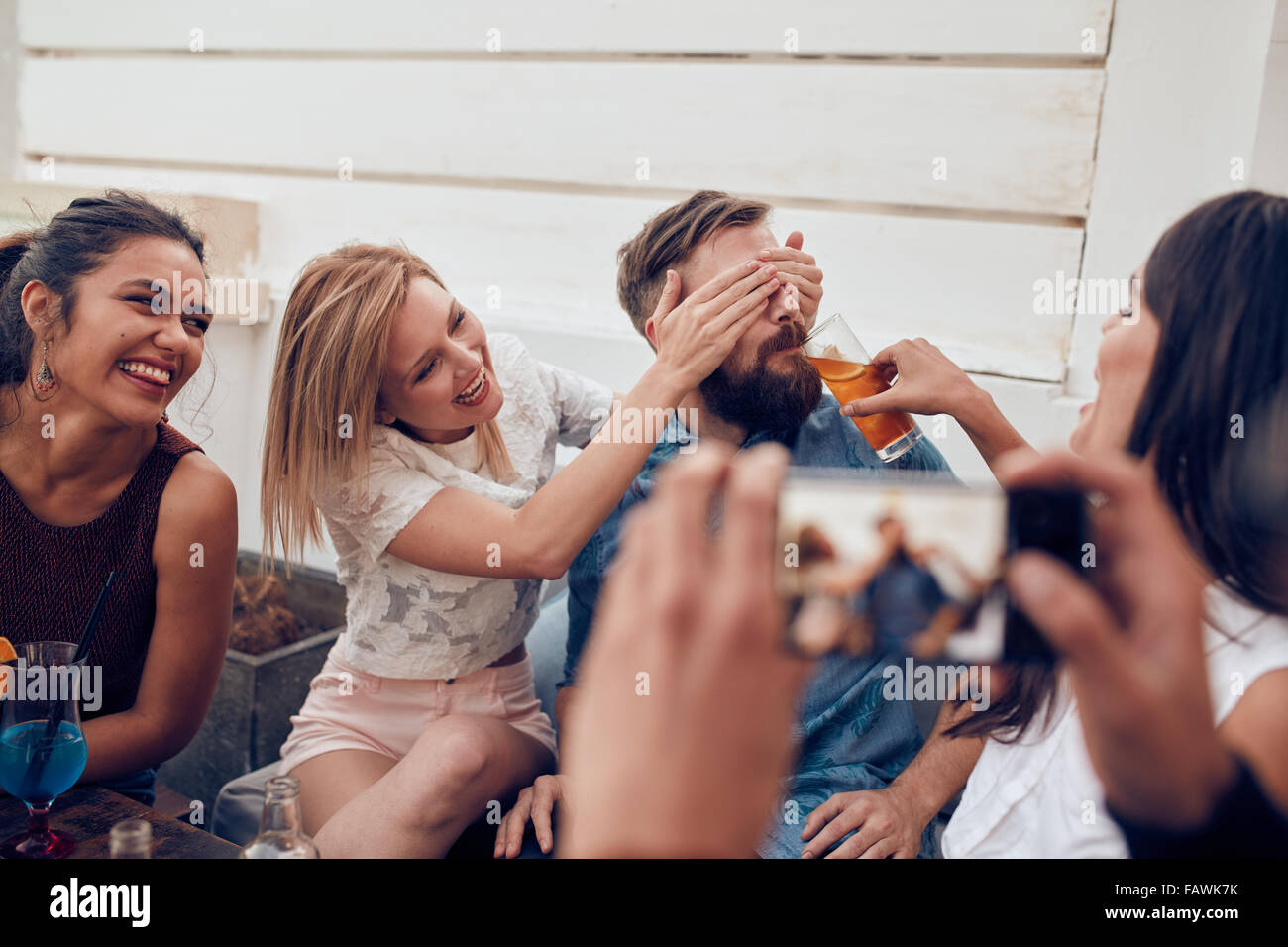 Young friends having fun at party being photographed with mobile phone. Young people sitting together enjoying party with one wo Stock Photo