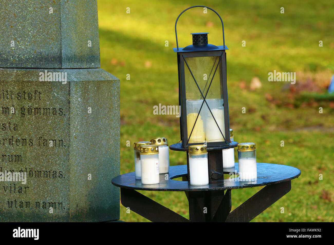 Ronneby, Sweden - December 29, 2015: Small iron table with lanterns on top. Beside is part of memorial tombstone for unnamed per Stock Photo