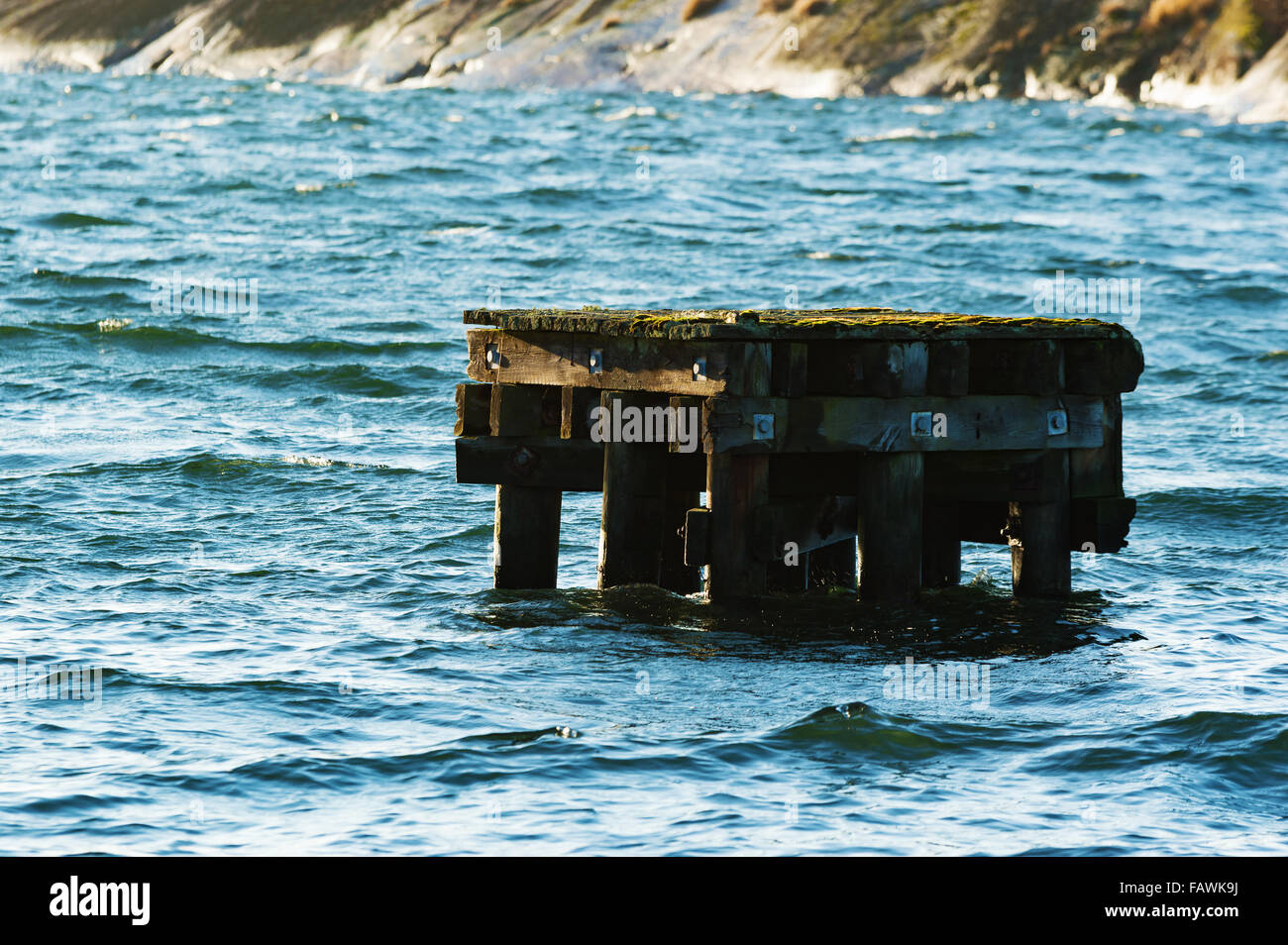 An old wooden platform in the sea close to a harbor. The platform helps to keep ships and boats in place when moored. Lichen cov Stock Photo