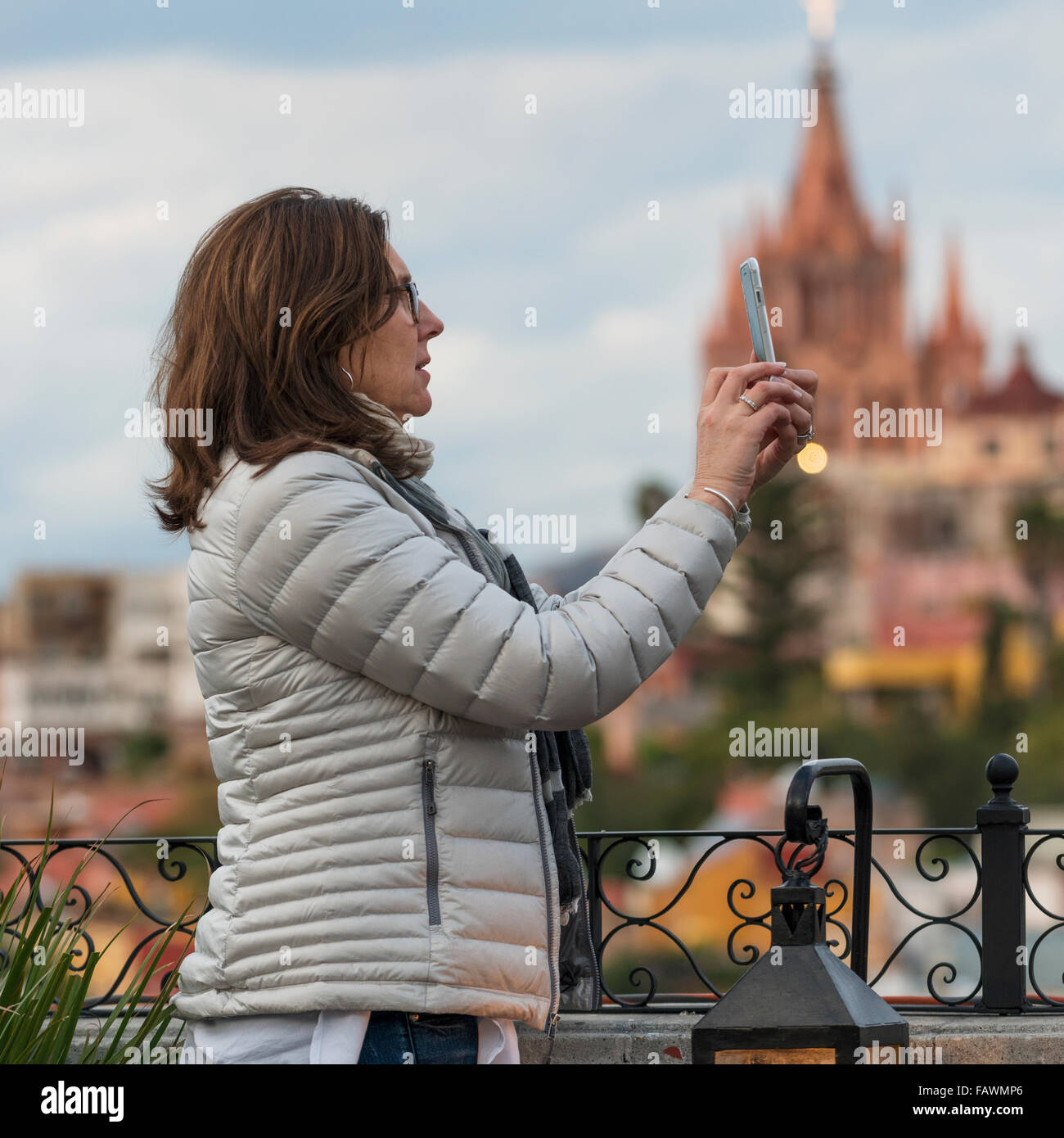 Woman taking a photograph with a smart phone and a church in the distance; San Miguel de Allende, Guanajuato, Mexico Stock Photo