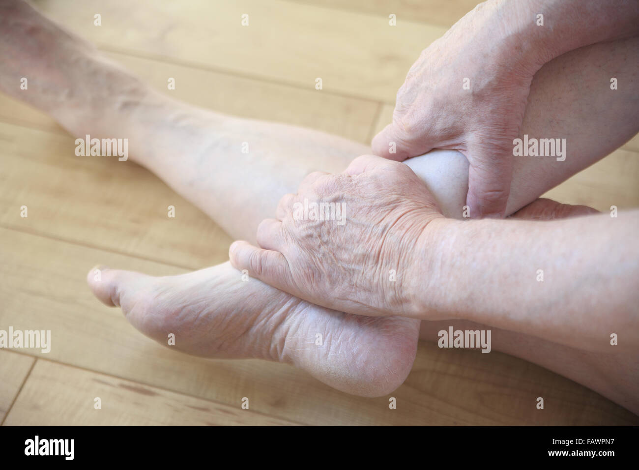 Senior man seated on floor holds an ankle with both hands. Stock Photo