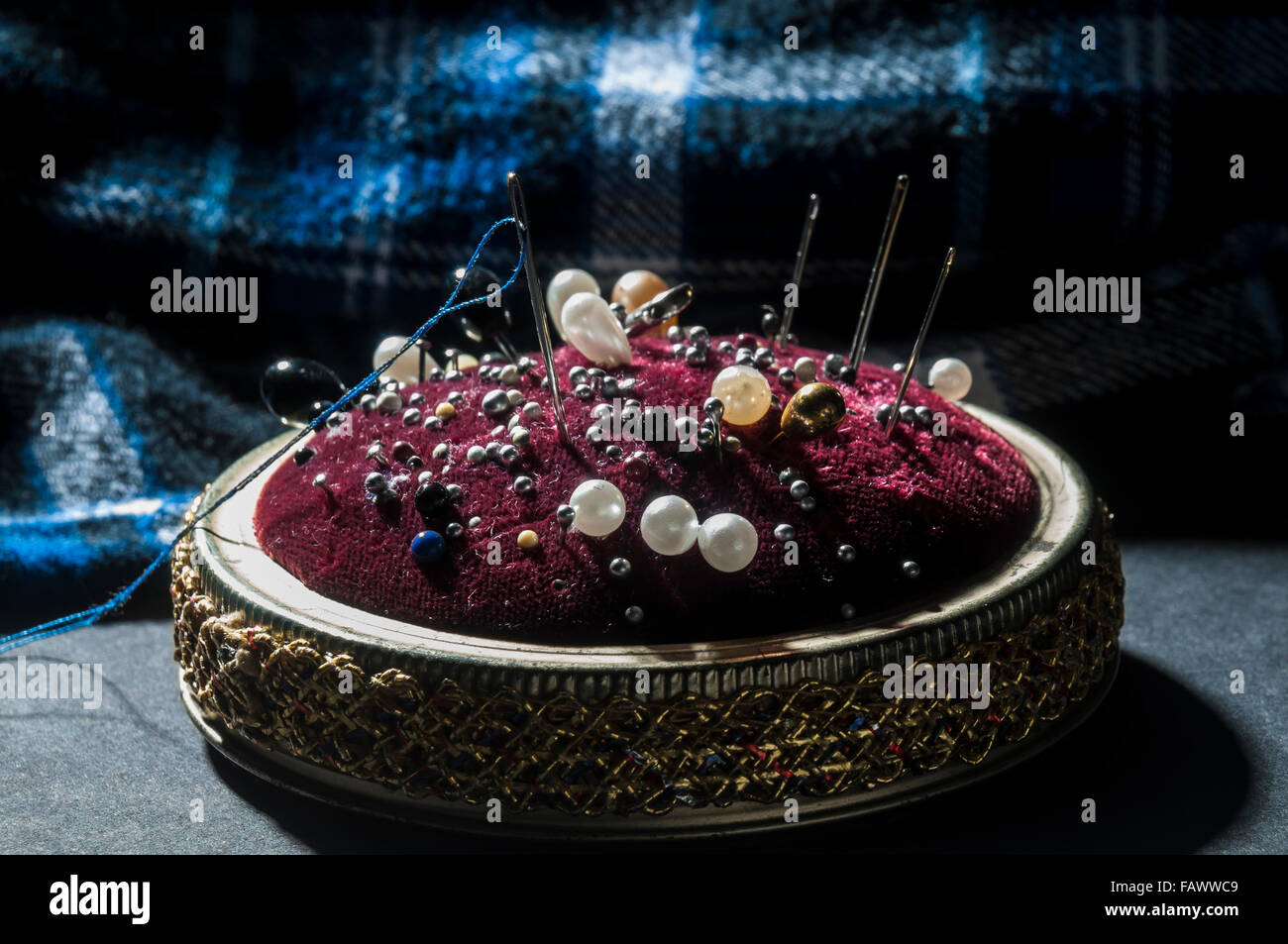 An old pincushion with pins, needles, and thread in front of cloth