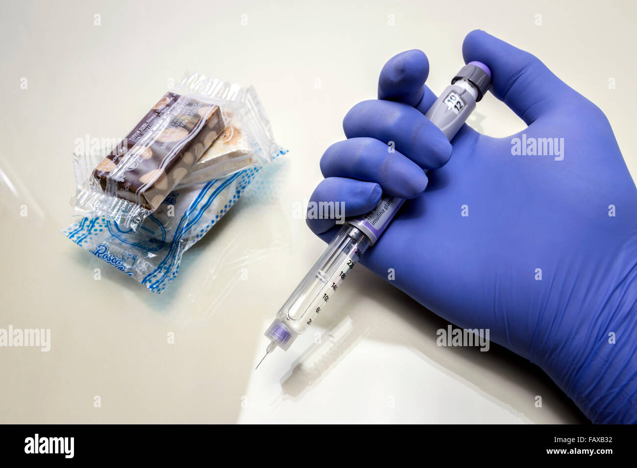 Blue-gloved hand holds a syringe of insulin together with some sweets and packaged cakes. Diabetes concept Stock Photo