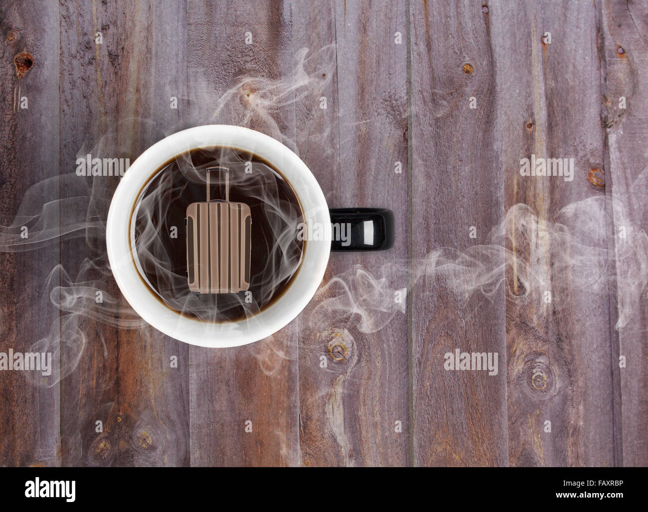 Dreaming of travel over hot cup of coffee concept - mug placed on wooden table with hot black coffee and suitcase Stock Photo