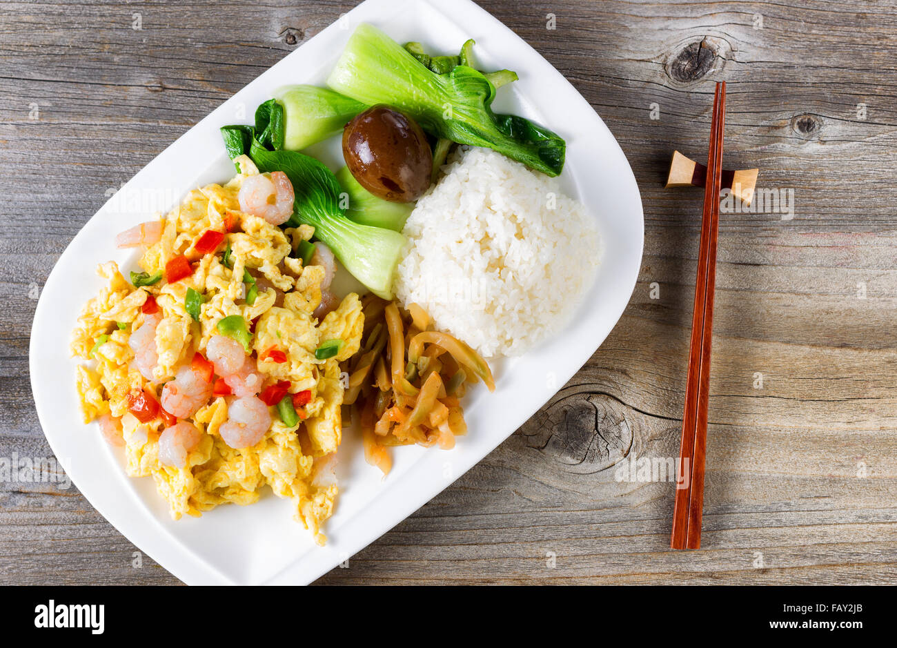 Top view of freshly cooked egg and shrimp dish with bok choy, soy sauce egg, cucumber, rice and chopsticks in holder on rustic w Stock Photo