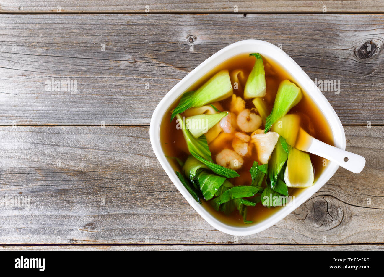Top view Chinese soup dish with shrimp, fish, bok choy, and spoon on rustic wood. Stock Photo